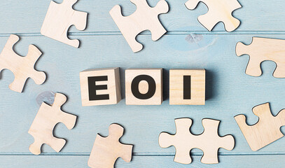 Obraz premium Blank puzzles and wooden cubes with the text EOI Expression of Interest lie on a light blue background.