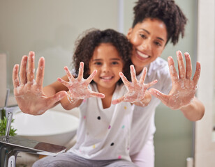 A mom teaching child to clean their hands, using soap and water in the bathroom to destroy germs to...