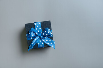 Black gift box with bow flat lay on grey background. View from above. Copy space
