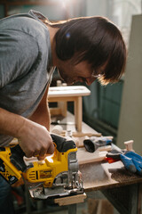 A wood-worker using a jigsaw to cut out a curve in a work piece of pine.