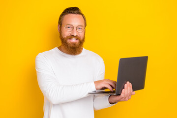 Photo of cheerful smart man hold use wireless netbook write email isolated on yellow color background