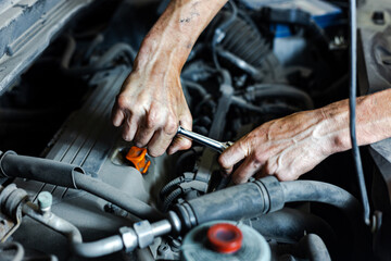 An auto mechanic works with a car engine in the mechanics' garage. Car repair close-up. An authentic close-up shot of an auto mechanic's hands.