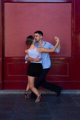 Boy in a suit and girl in shorts and a white t-shirt Couple dancing Tango, with a red background.