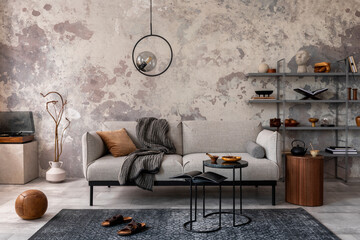 Loft style of modern apartment with grey design sofa, marble coffee table, bookstand, pedant lamp, carpet, decoration and elegant accessories . Concrete grunge wall. Template.	