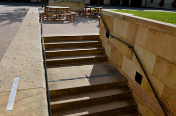 beige staircase descends under the terrain of a grassy yard with park paths. the walls are made of...