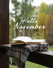 A cup of tea, a book and a warm plaid on the terrace in the autumn garden with Hello November lettering