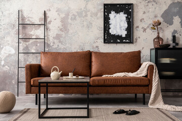 Interior design of loft industrial apartment with mock up poster frame, brown sofa, coffee table, black commode and stylish personal accessories. Concrete gray wall. Home decor. Template. 