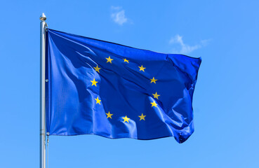 The flag of Europe, the symbol of the European Union and the Council of Europe, is a blue banner with 12 yellow stars forming a circle in the middle on a background of blue sky during the summer day