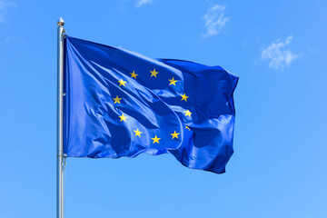 The flag of Europe, the symbol of the European Union and the Council of Europe, is a blue banner with 12 yellow stars forming a circle in the middle on a background of blue sky during the summer day