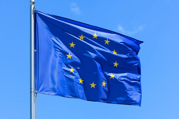 The flag of Europe, the symbol of the European Union and the Council of Europe, is a blue banner with 12 yellow stars forming a circle in the middle on a background of blue sky during the summer day
