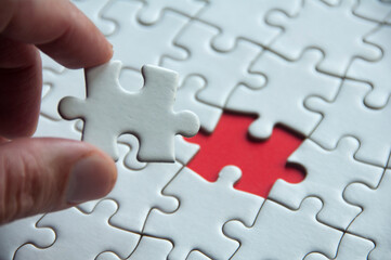Hand holding white jigsaw puzzle on red cover background with customizable space for text or idea....