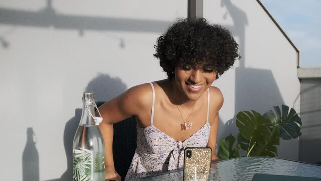 Transgender woman having a video call on a mobile phone while relaxing sitting on the terrace outdoors.