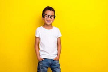 Photo of cool small boy wear white t-shirt eyewear jeans isolated on yellow color background
