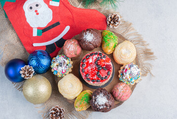 An assortment of desserts on a wooden board adorned with baubles, stocking and pine cones on marble background