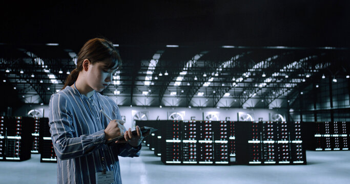 A Young Female Use Tablet While Worke in Server Room in Contemporary Data Center. IT Technician. Cloud Storage Technology, Database, Engineering