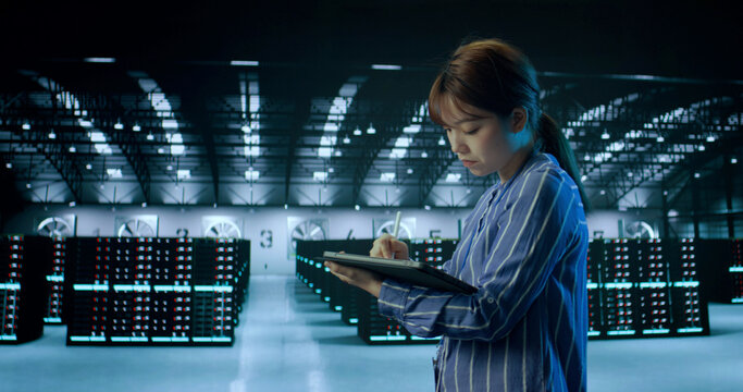 A Young Female Using Tablet While Working in Server Room in Contemporary Data Center. IT Technician. Cloud Storage Technology, Database, Engineering