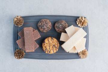 Stacks of wafers and cookies on a navy board with pine cones on marble background