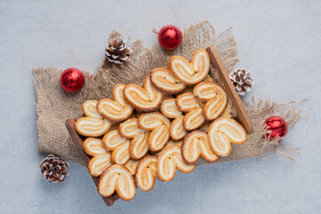 Bunch of christmas ornaments around flaky cookies piled in a wooden basket on marble background
