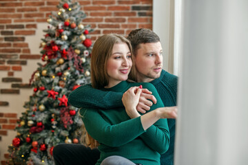 Couple hugging on windowsill and looking out window. Concept of family, Christmas and winter season.
