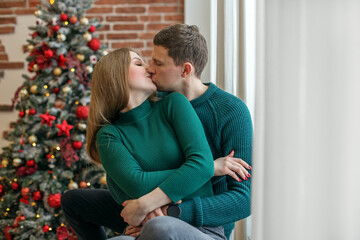 Loving couple embrace and kiss on the windowsill. Concept of family, Christmas and winter season