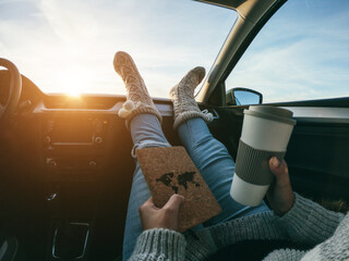 Woman reading book and drinking coffee inside car on winter day - Travel concept - Focus on warm socks