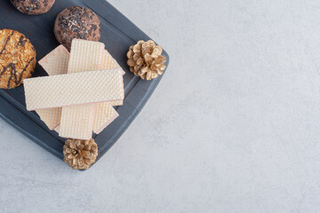 Cookies next to a stack of wafers on a navy board with pine cones on marble background