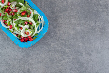 Sliced greens, onions and pomegranate seeds on blue plate