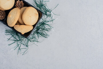 Pile of cookeis in a black platter adorned with artificial pine leaves on marble background