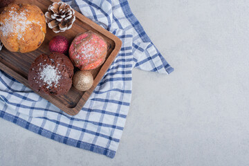 Wooden tray with cupcakes on a towel, adorned with pine cones and christmas baubles on marble background