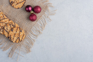 Crispy cookies and christmas baubles on a piece of cloth on marble background