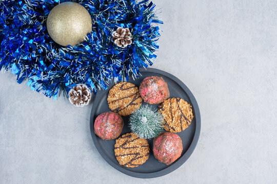 Small tray of cookies next to a bundle of christmans decorations on marble background