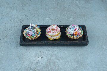 Cupcakes and donuts on a black tray on marble background
