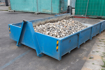 Blue metal construction trash dumpsters container, full of paving stones for street reconstruction.