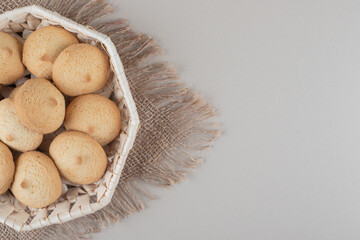 Crumbly cookies in a white basket on a piece of cloth on marble background