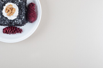 Chocolate cake and red pine cones on a platter on marble background