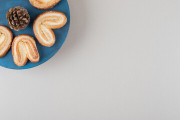 Pine cone surrounded by flaky cookies on a platter on marble background