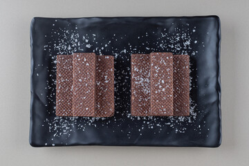 Chocolate coated wafers stacked on a black platter on marble background