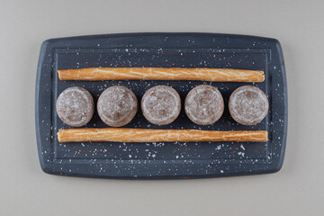 Small cookies and stick crackers on navy platter on marble background