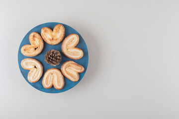 Pine cone surrounded by flaky cookies on a platter on marble background