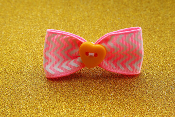 a pink bow with a yellow button in the middle for dogs stands on a gold background.  side view.  dog accessory