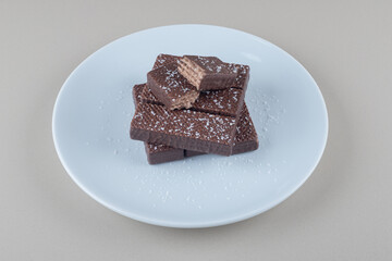 Chocolate coated wafers stacked on a white platter on marble background