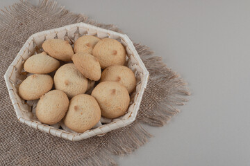 Crumbly cookies in a white basket on a piece of cloth on marble background