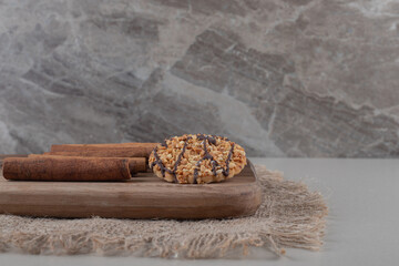A cookie and cinnamon sticks on a wooden board on marble background