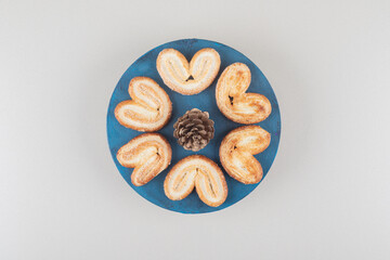 Pine cone surrounded by flaky cookies on a platter on marble background