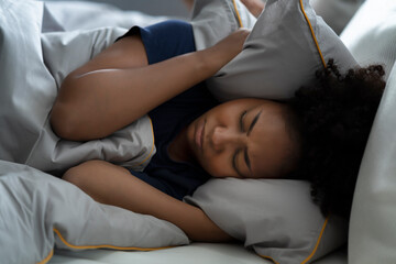 Young black woman uses pillow to cover her ears, feeling annoying her husband snoring loudly and making her awake from sleeping.