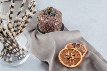 Small cake, dried lemon slices and a bundle of straw pipes on marble background