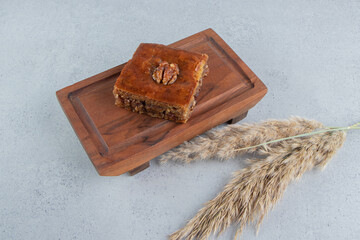 Bakhlava on a small board next to a stalk of feather grass on marble background