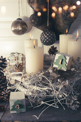 Four white candles on an old wooden background. Atmospheric Christmas decorations with self-made advent calendar and consistent natural elements. Branches with pine cones and magic bokeh lights.