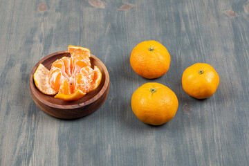 Bowl of segments with whole tangerines on marble background