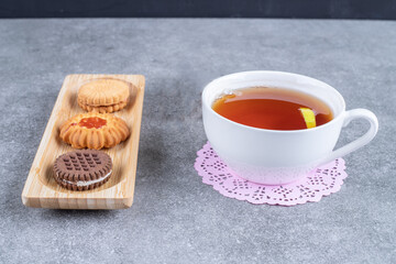 Plate of various biscuits with cup of tea on marble background